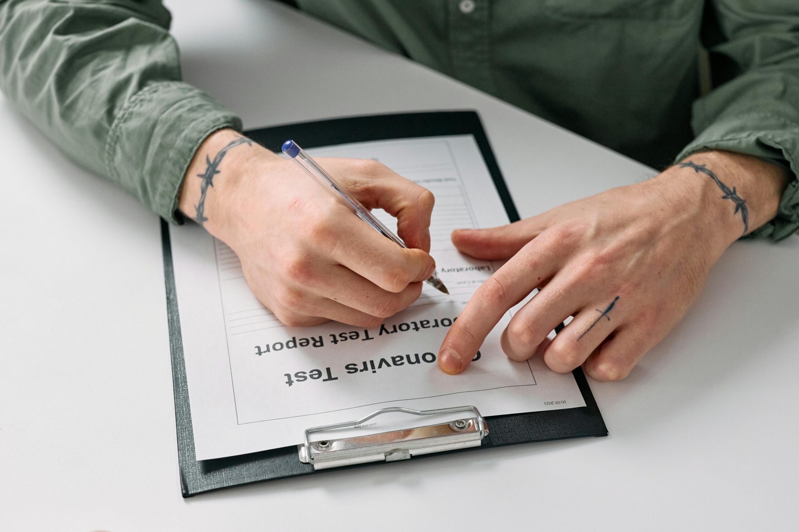Tattoos on Hands of Man Writing on Notepad